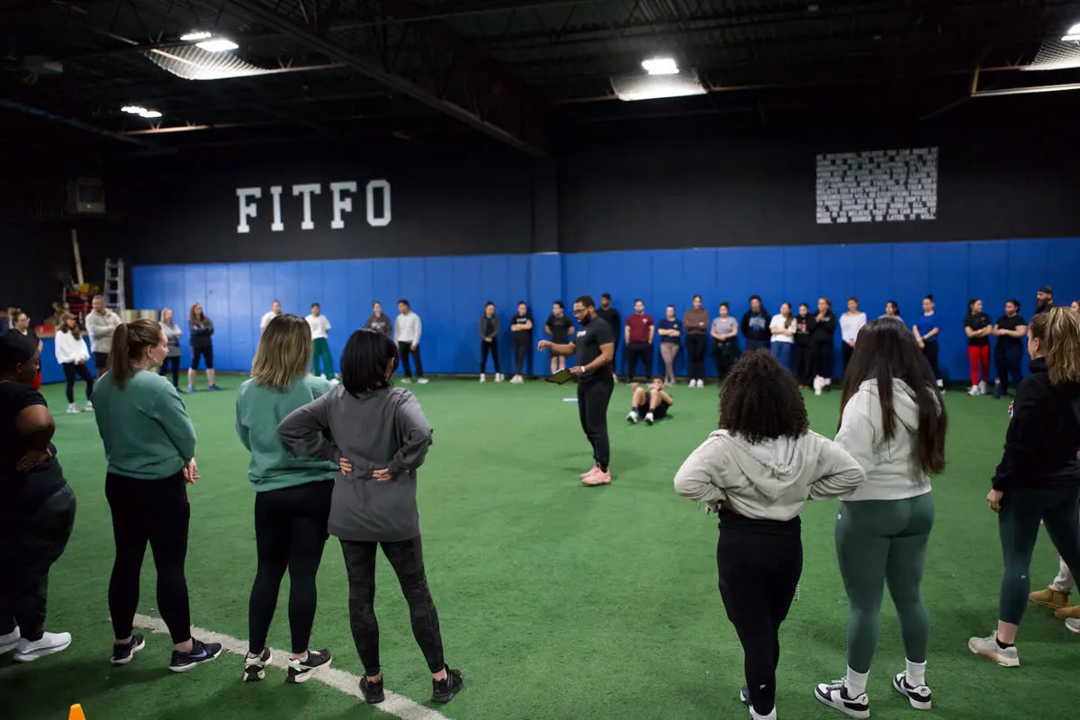 People standing in a circle on gym turf while a BTSG leader speaks in the center